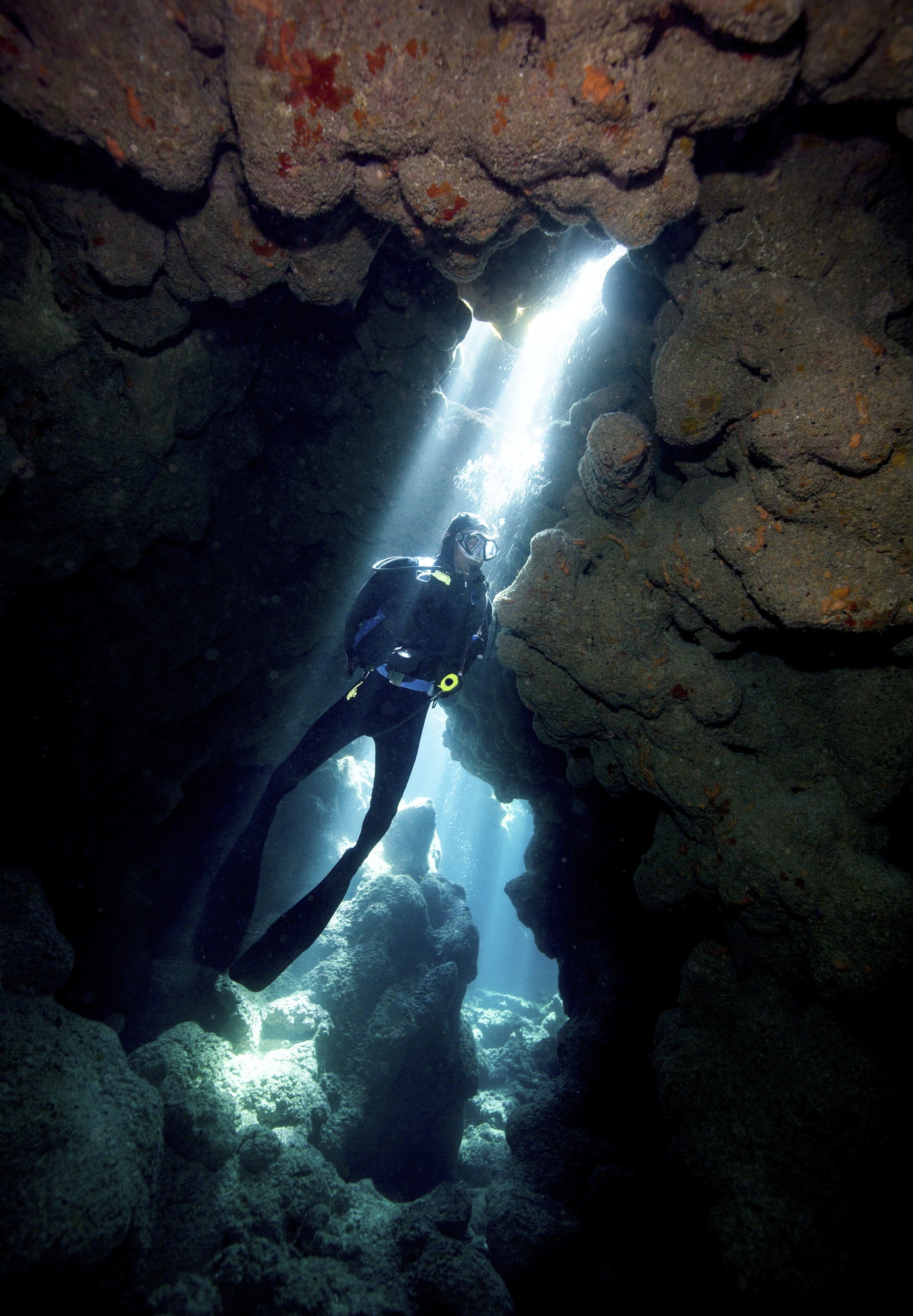 Crepuscular rays illuminate a scuba diver at Coral Caverns dive site.,Diver in Reef Crevice.
