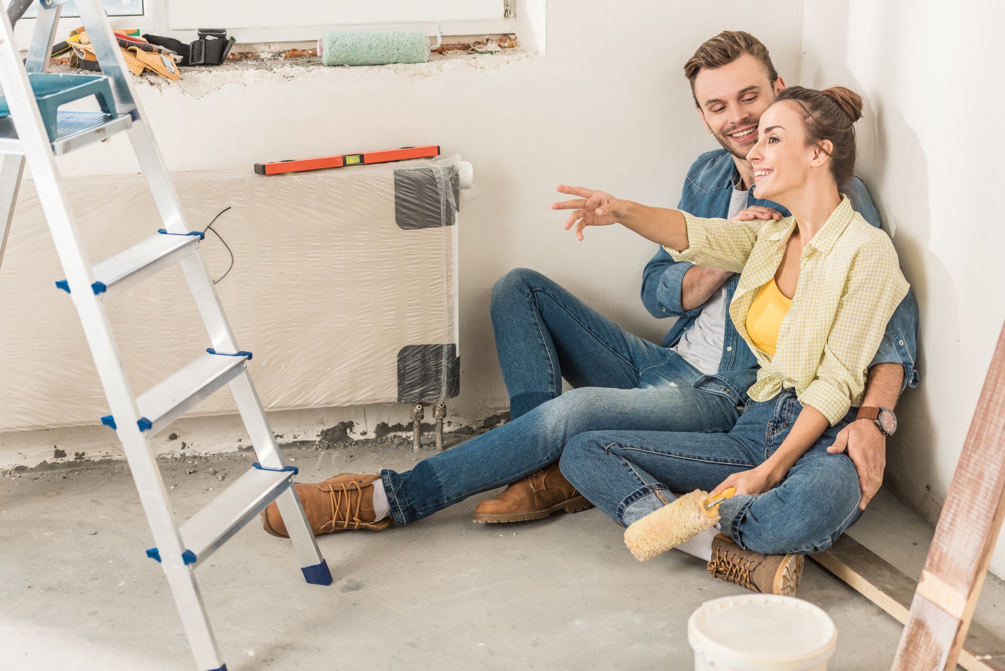 happy young couple sitting on floor and looking away during home improvement